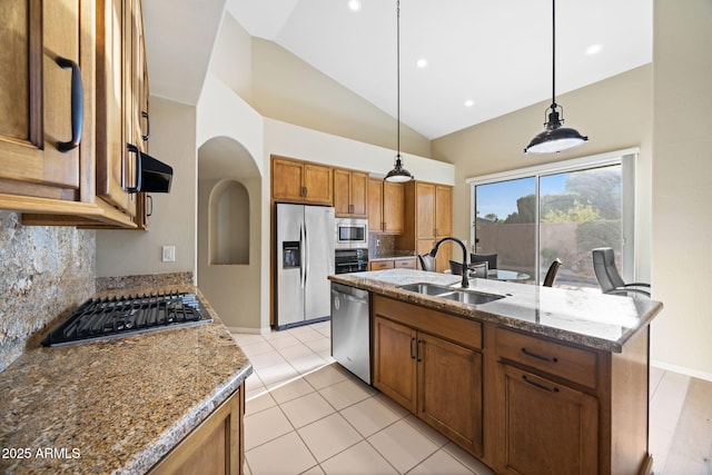 11816 E Terra Dr, Scottsdale, AZ 85259 - kitchen featuring appliances with stainless steel finishes, decorative backsplash, brown cabinetry, a kitchen island with sink, and hanging light fixtures