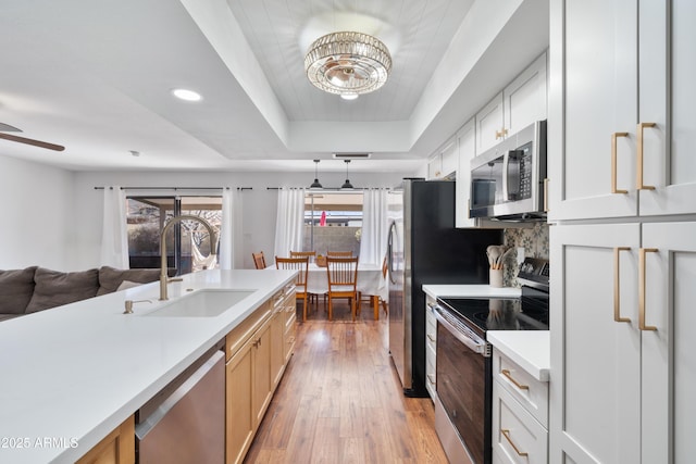 kitchen featuring wood finished floors, a sink, stainless steel appliances, light countertops, and a raised ceiling