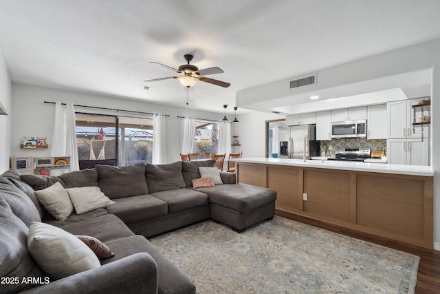 living room with visible vents, a healthy amount of sunlight, ceiling fan, and dark wood-style flooring