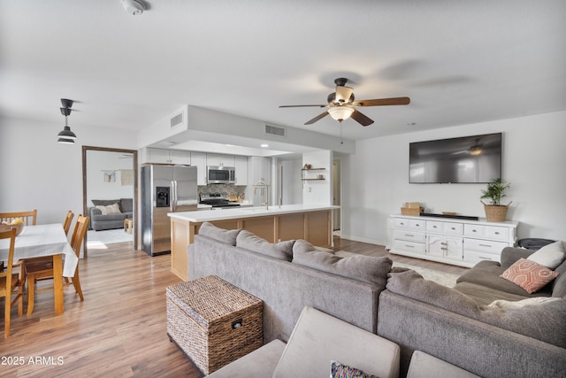 living area with visible vents, light wood finished floors, and ceiling fan