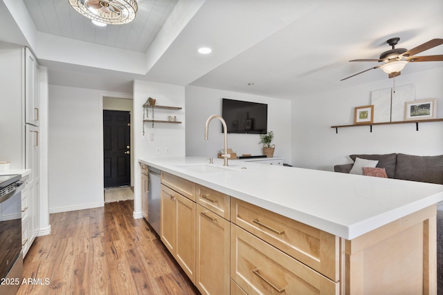 kitchen featuring wood finished floors, a peninsula, a sink, light brown cabinetry, and stainless steel dishwasher