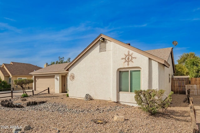 view of front of house featuring an attached garage, a shingled roof, fence, and stucco siding