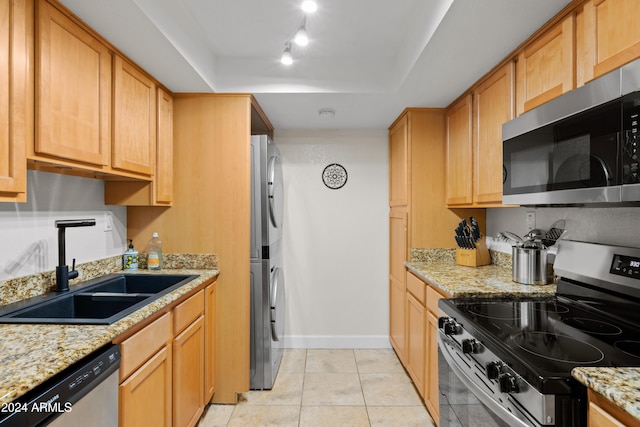 kitchen featuring light stone countertops, sink, rail lighting, stacked washing maching and dryer, and appliances with stainless steel finishes