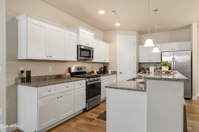 kitchen with light wood-type flooring, appliances with stainless steel finishes, white cabinetry, sink, and an island with sink