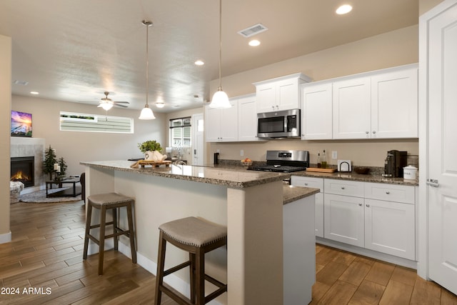 kitchen with a high end fireplace, appliances with stainless steel finishes, an island with sink, dark wood-type flooring, and ceiling fan