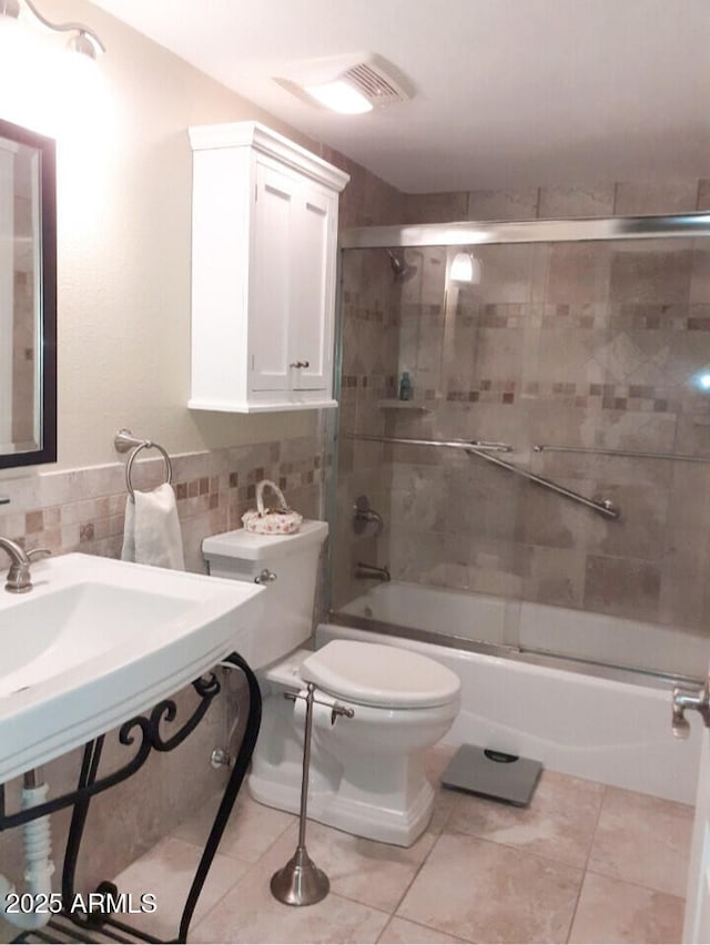 full bath with enclosed tub / shower combo, toilet, tile patterned floors, tile walls, and a wainscoted wall