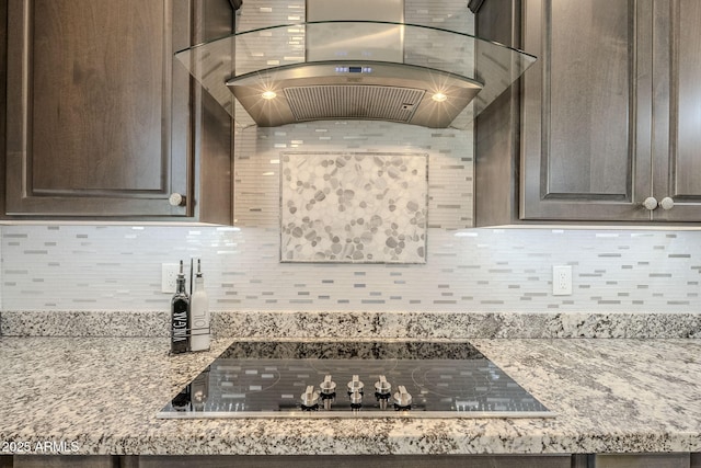 kitchen with light stone counters, black electric stovetop, decorative backsplash, dark brown cabinets, and wall chimney exhaust hood