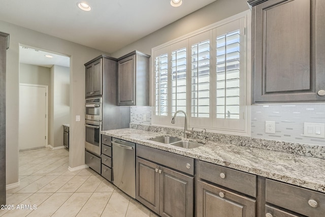 kitchen featuring light tile patterned floors, tasteful backsplash, light stone counters, stainless steel appliances, and a sink