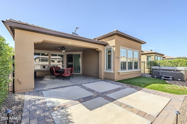 rear view of house featuring outdoor dining area, a patio, stucco siding, a hot tub, and a ceiling fan