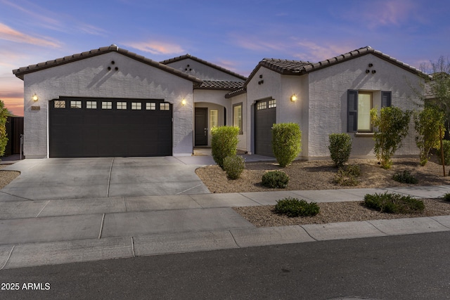 mediterranean / spanish house with an attached garage, driveway, a tile roof, and stucco siding