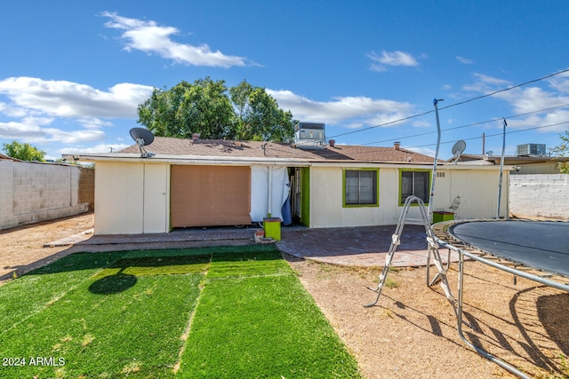 back of property with a yard, cooling unit, and a trampoline