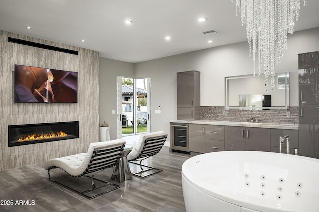 kitchen with gray cabinets, a fireplace, tasteful backsplash, a notable chandelier, and beverage cooler