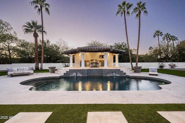 pool at dusk featuring pool water feature and a patio area