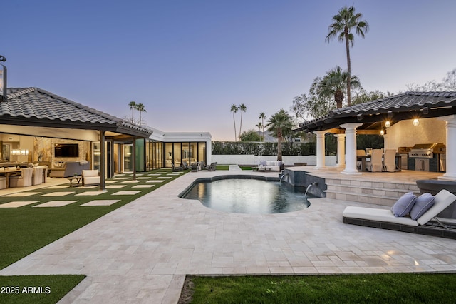 pool at dusk with pool water feature, an outdoor kitchen, area for grilling, and a patio area