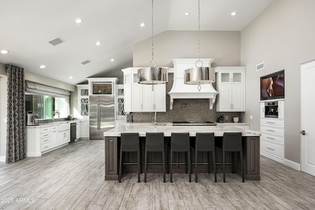 kitchen with tasteful backsplash, stainless steel appliances, extractor fan, a large island with sink, and decorative light fixtures