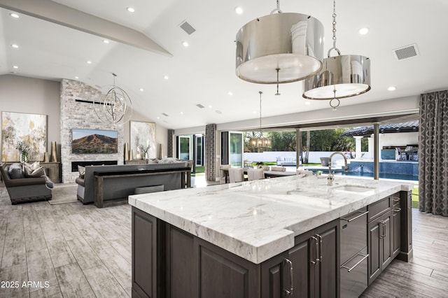 kitchen featuring a fireplace, a large island with sink, lofted ceiling, and sink