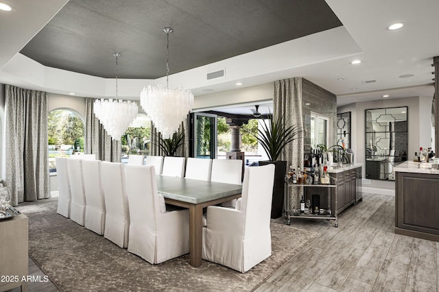 dining space featuring light wood-type flooring, a raised ceiling, and a notable chandelier