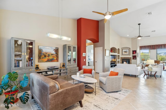 living area featuring a ceiling fan, high vaulted ceiling, a glass covered fireplace, arched walkways, and light tile patterned floors