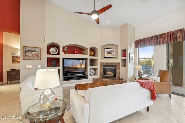 living room with built in features, high vaulted ceiling, light tile patterned floors, ceiling fan, and a fireplace