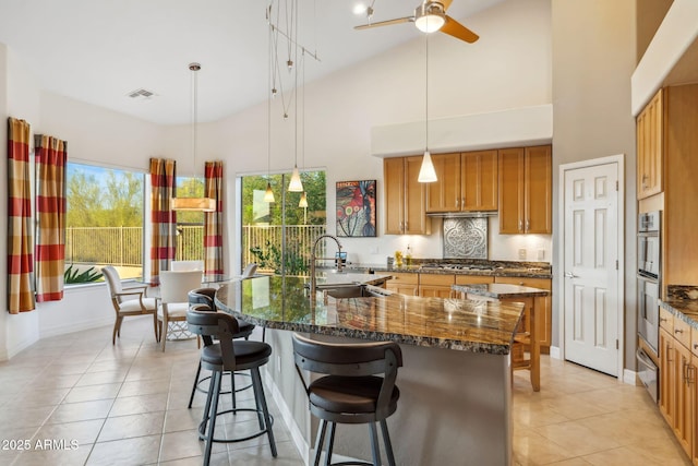 kitchen with a sink, a warming drawer, light tile patterned floors, brown cabinetry, and high vaulted ceiling