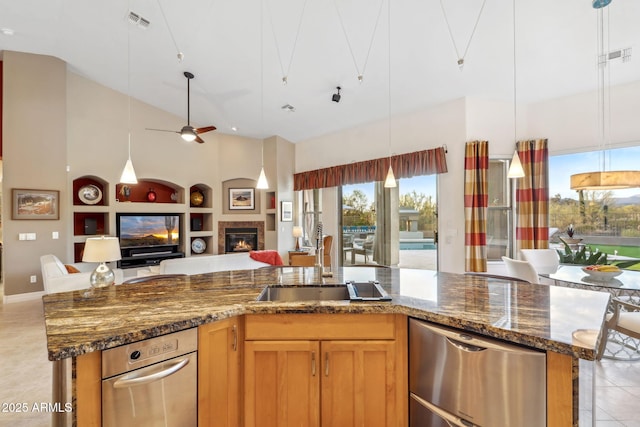 kitchen featuring open floor plan, dishwasher, a ceiling fan, built in shelves, and a glass covered fireplace