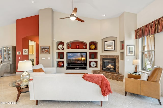living area with high vaulted ceiling, built in features, a tiled fireplace, ceiling fan, and arched walkways