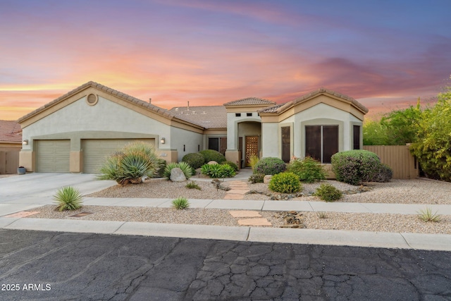 mediterranean / spanish house with an attached garage, stucco siding, concrete driveway, a tile roof, and fence
