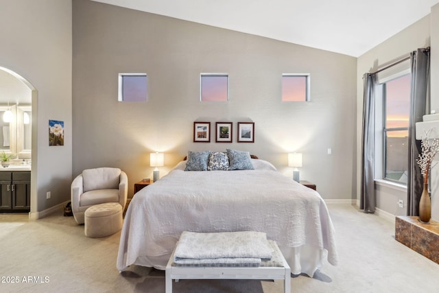 bedroom featuring vaulted ceiling, light carpet, arched walkways, and baseboards