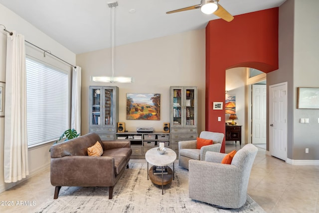 living area with arched walkways, ceiling fan, light tile patterned floors, high vaulted ceiling, and baseboards