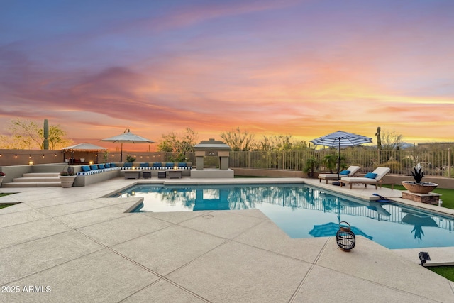 pool at dusk with outdoor lounge area, a patio area, and a fenced backyard