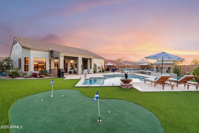 rear view of property with a putting green, a patio area, a tiled roof, and stucco siding