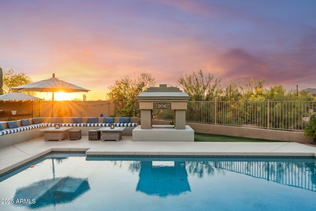 pool at dusk with outdoor lounge area, fence, and a patio area