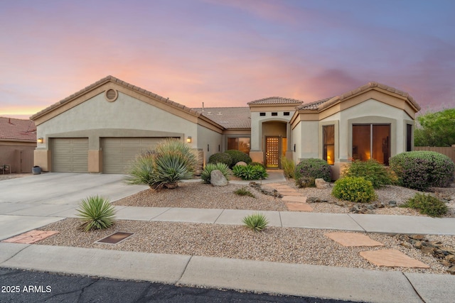 mediterranean / spanish home with an attached garage, concrete driveway, stucco siding, and a tiled roof