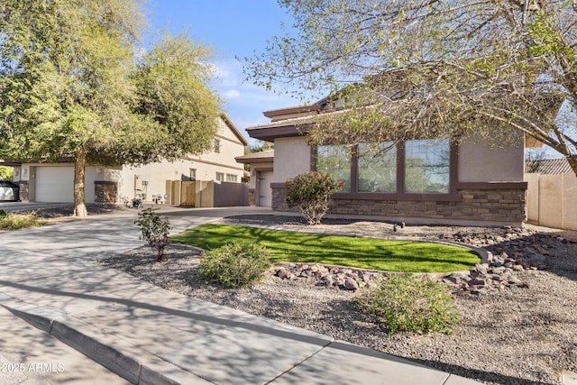 view of front of home with stucco siding, driveway, stone siding, and fence
