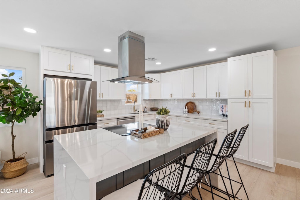 kitchen featuring a center island, white cabinets, light wood-type flooring, light stone counters, and island exhaust hood