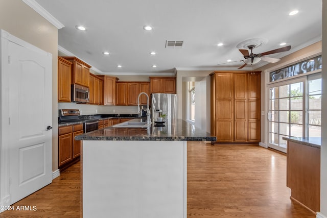 kitchen featuring sink, crown molding, light wood-type flooring, appliances with stainless steel finishes, and an island with sink