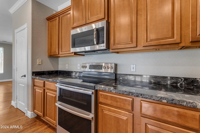 kitchen with crown molding, stainless steel appliances, light hardwood / wood-style floors, and dark stone countertops