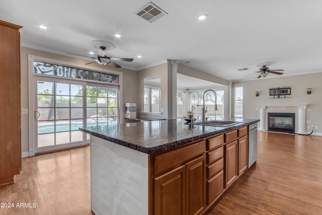 kitchen featuring dishwasher, sink, dark stone countertops, crown molding, and a center island with sink