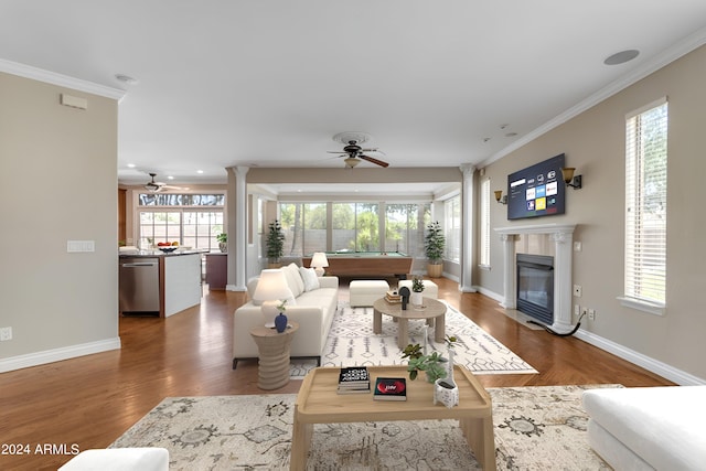 living room featuring decorative columns, crown molding, dark wood-type flooring, and ceiling fan