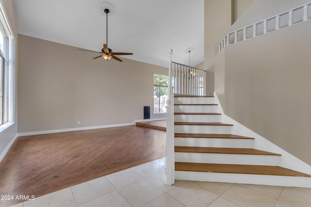 stairway with tile patterned flooring, ceiling fan with notable chandelier, and high vaulted ceiling