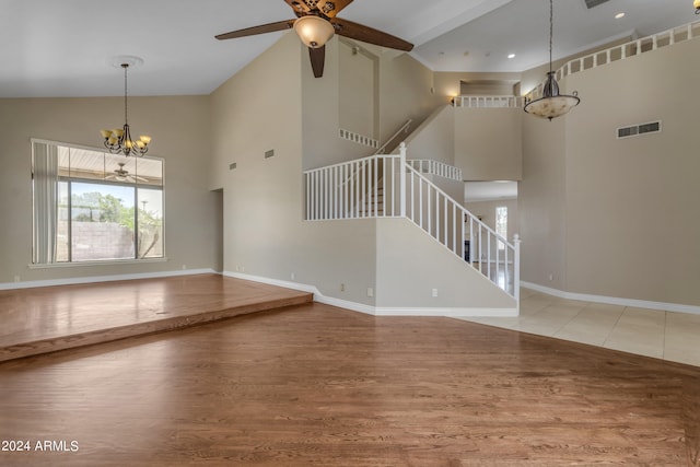 unfurnished living room featuring ceiling fan with notable chandelier, light hardwood / wood-style floors, and a high ceiling