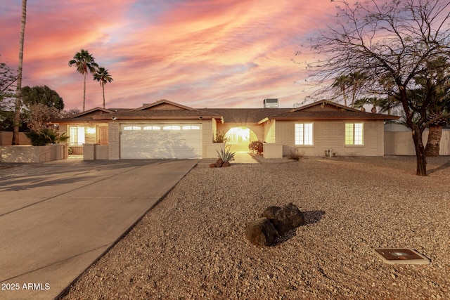 single story home with concrete driveway, brick siding, fence, and an attached garage