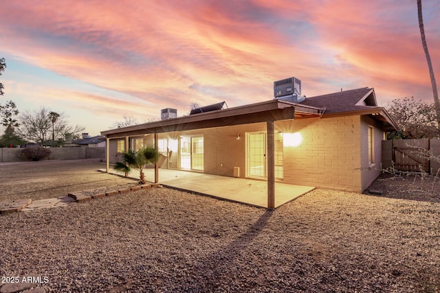 back of property at dusk featuring a patio area, brick siding, a fenced backyard, and central AC unit