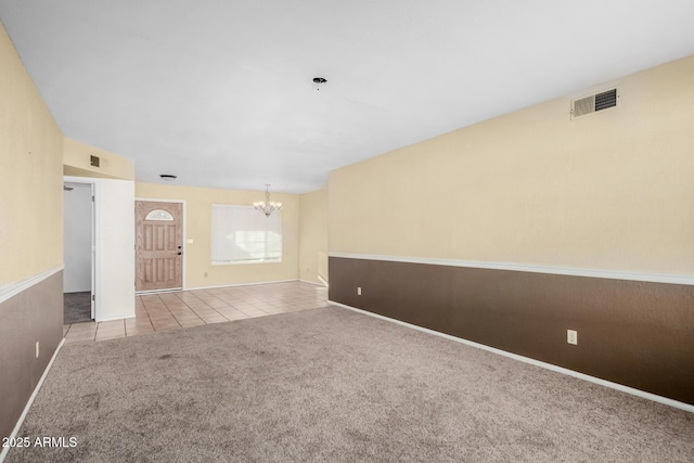 empty room featuring light tile patterned floors, visible vents, a notable chandelier, and light colored carpet