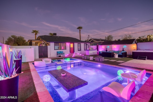 pool at dusk with an outdoor hot tub, a patio, and an outdoor hangout area