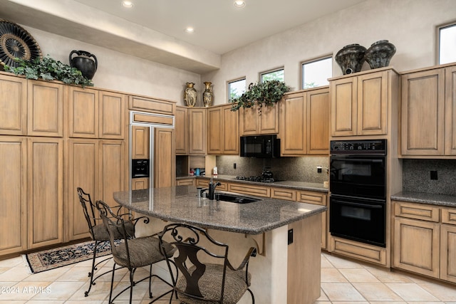 kitchen featuring backsplash, black appliances, an island with sink, a breakfast bar area, and light tile patterned flooring