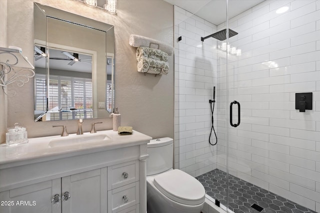 bathroom with ceiling fan, a stall shower, a textured wall, toilet, and vanity