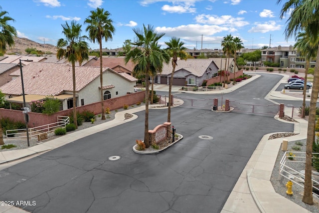 view of asphalt street featuring sidewalks, a residential view, curbs, a gated entry, and a gate