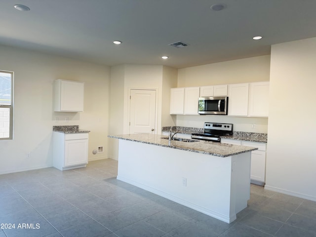 kitchen with stainless steel appliances, white cabinetry, and an island with sink