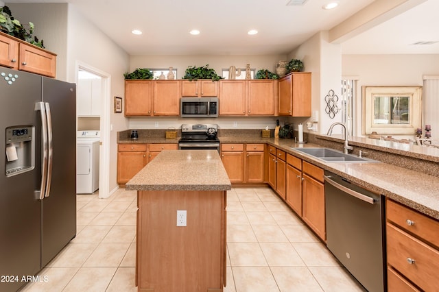 kitchen with appliances with stainless steel finishes, sink, light tile patterned floors, washer / dryer, and a kitchen island